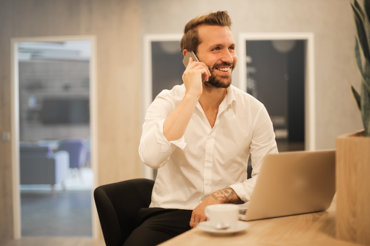 Un professionnel sourit au téléphone à son bureau, un ordinateur portable ouvert devant lui